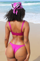 A woman wearing a shiny purple bikini   infront of the beach.