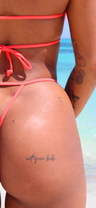 A close up of a woman’s red bikini bottom infront of the beach.