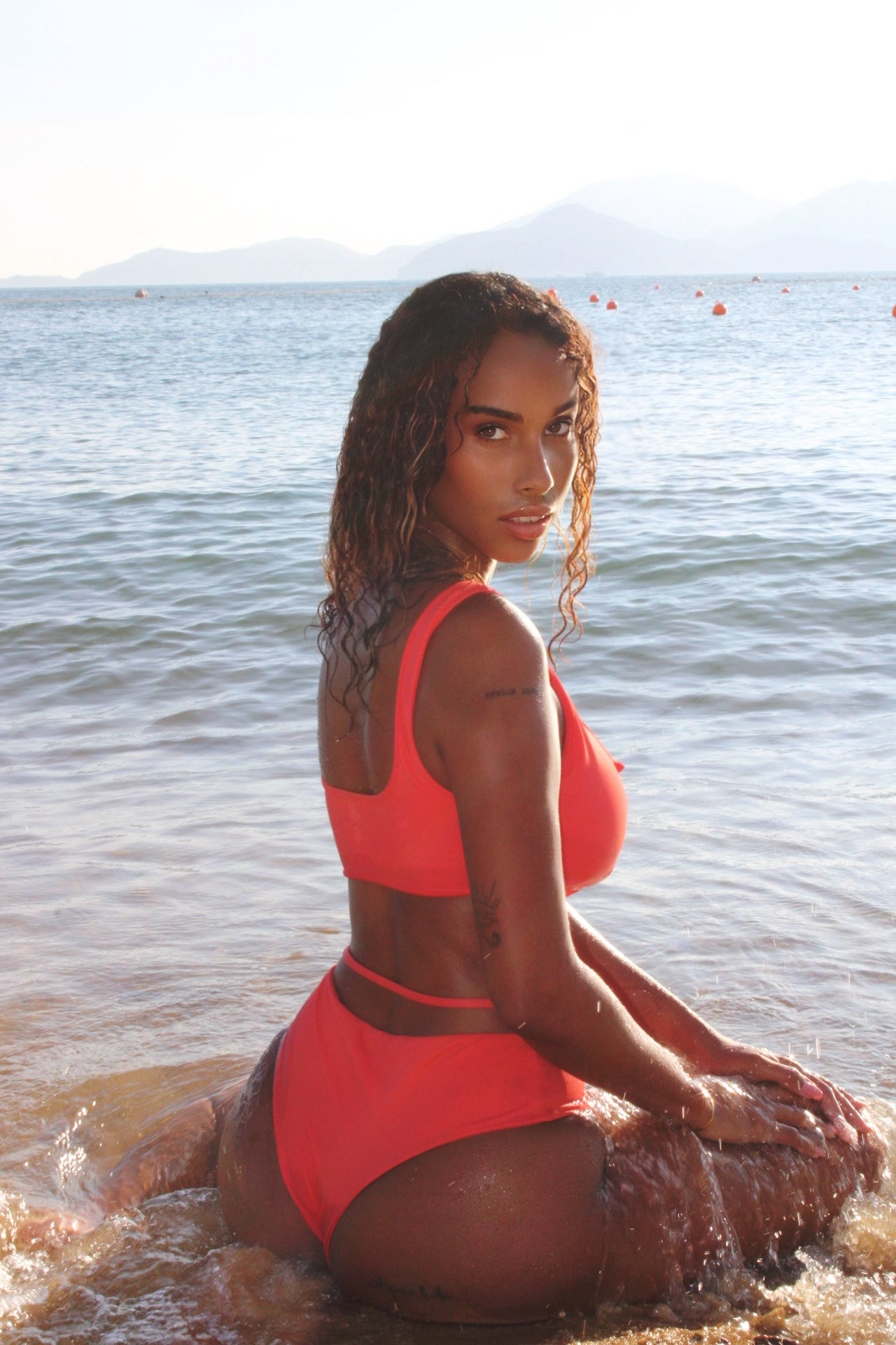 A woman in bared bikini sitting in the water on the beach.