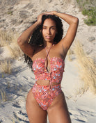 A woman standing on the beach wearing a multicolored floral swimsuit with an asymmetric cut-out neckline and ruching detail.