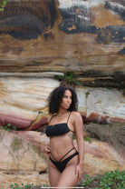 A black textured Leoprint bikini on a woman posing infront of a big natural stone.