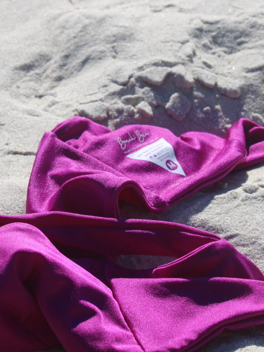 A shiny purple bikini top laying on the sandy beach.