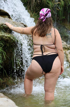 Person wearing a black bikini standing by a waterfall