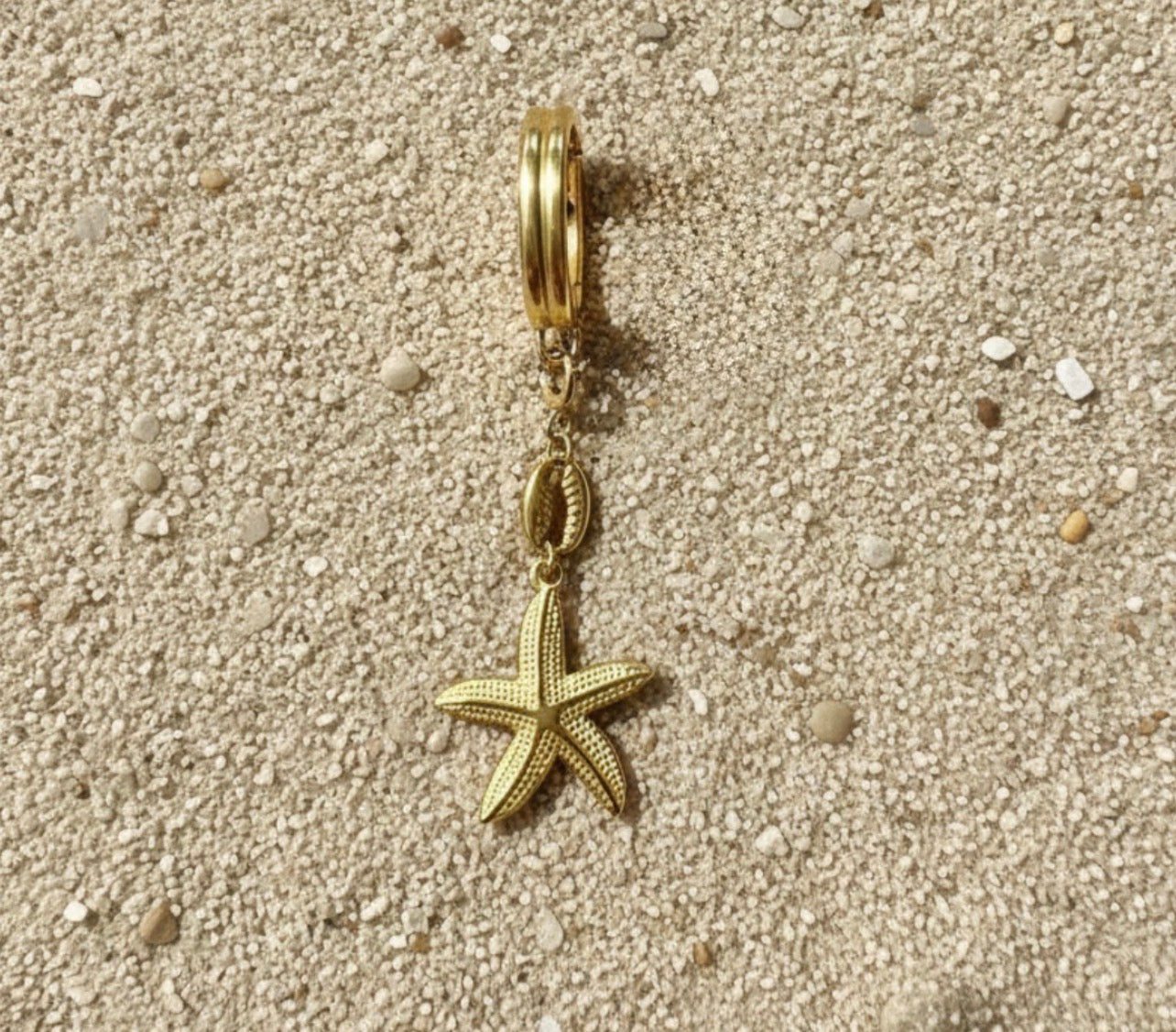 Gold charm with starfish design on a sandy background
