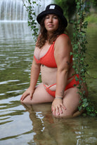 Woman in a red bikini sitting in water with a waterfall in the background