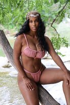 Woman in a pink bikini sitting by a natural water body with greenery.