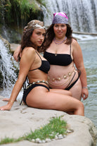Two women in black bikinis sitting by a waterfall.