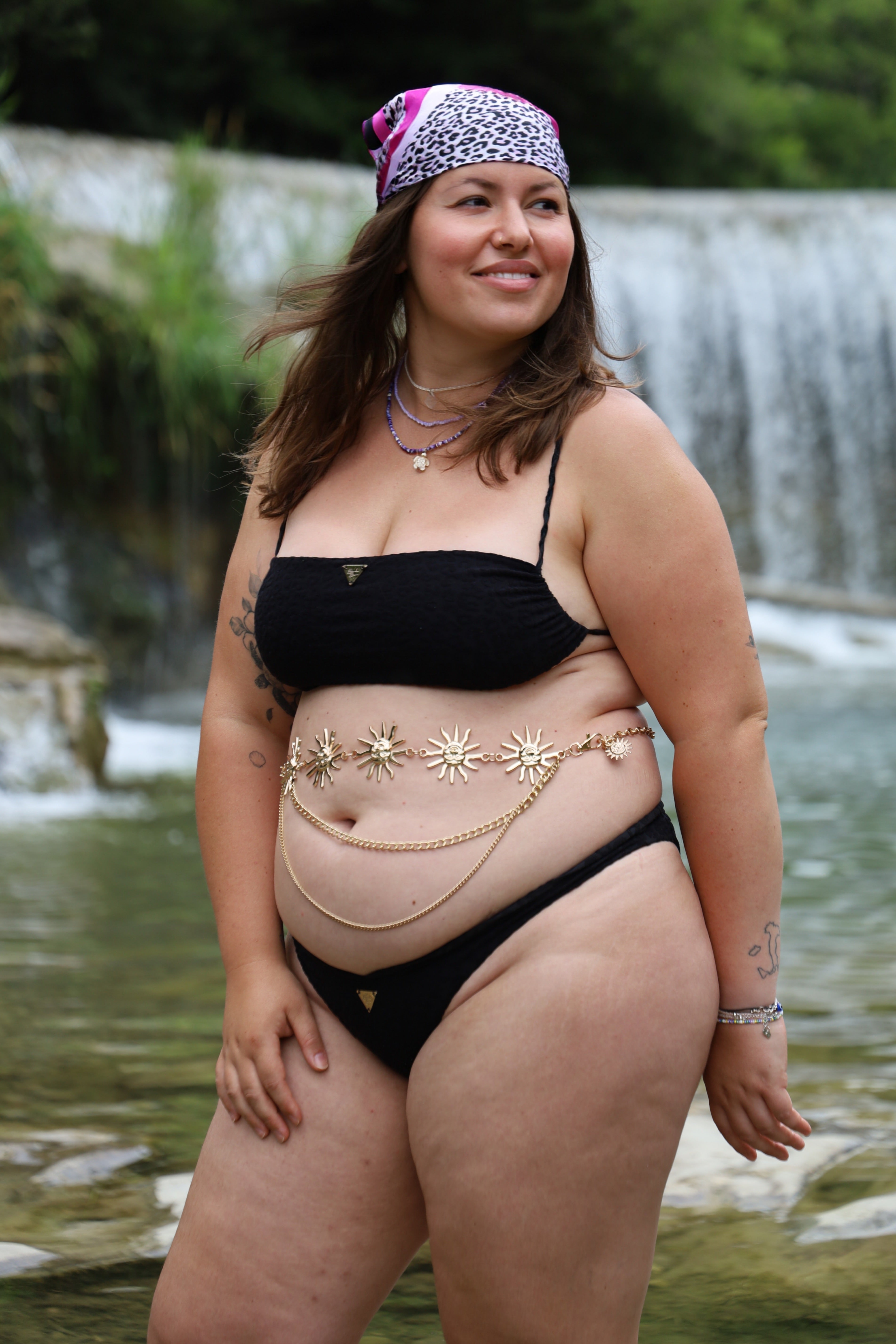 Woman in a black bikini standing by a waterfall