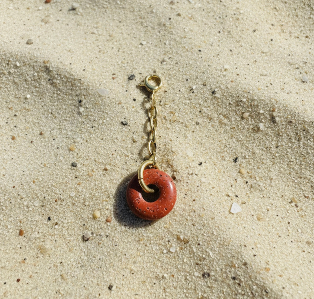 Bikini pendant with a red circular charm on a sandy surface