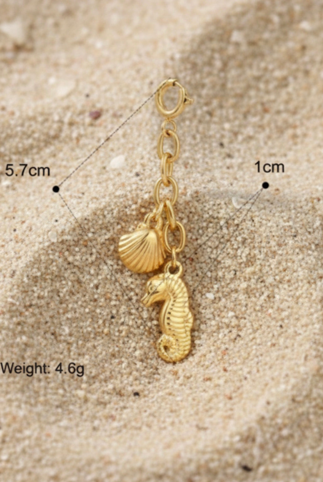 Gold charm with seahorse and shell design on sand, with measurements and weight displayed.