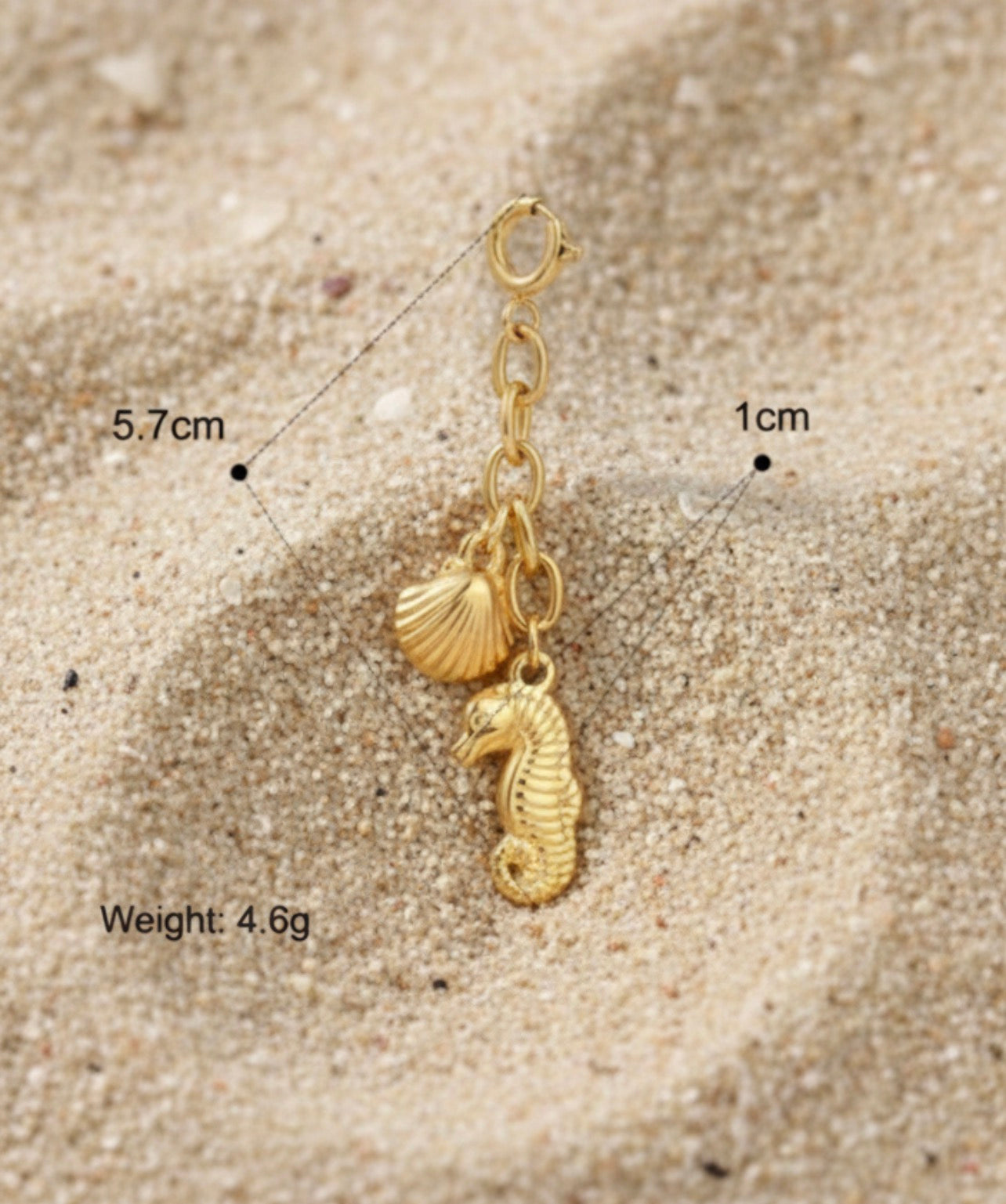Gold charm with seahorse and shell design on sand, with measurements and weight displayed.
