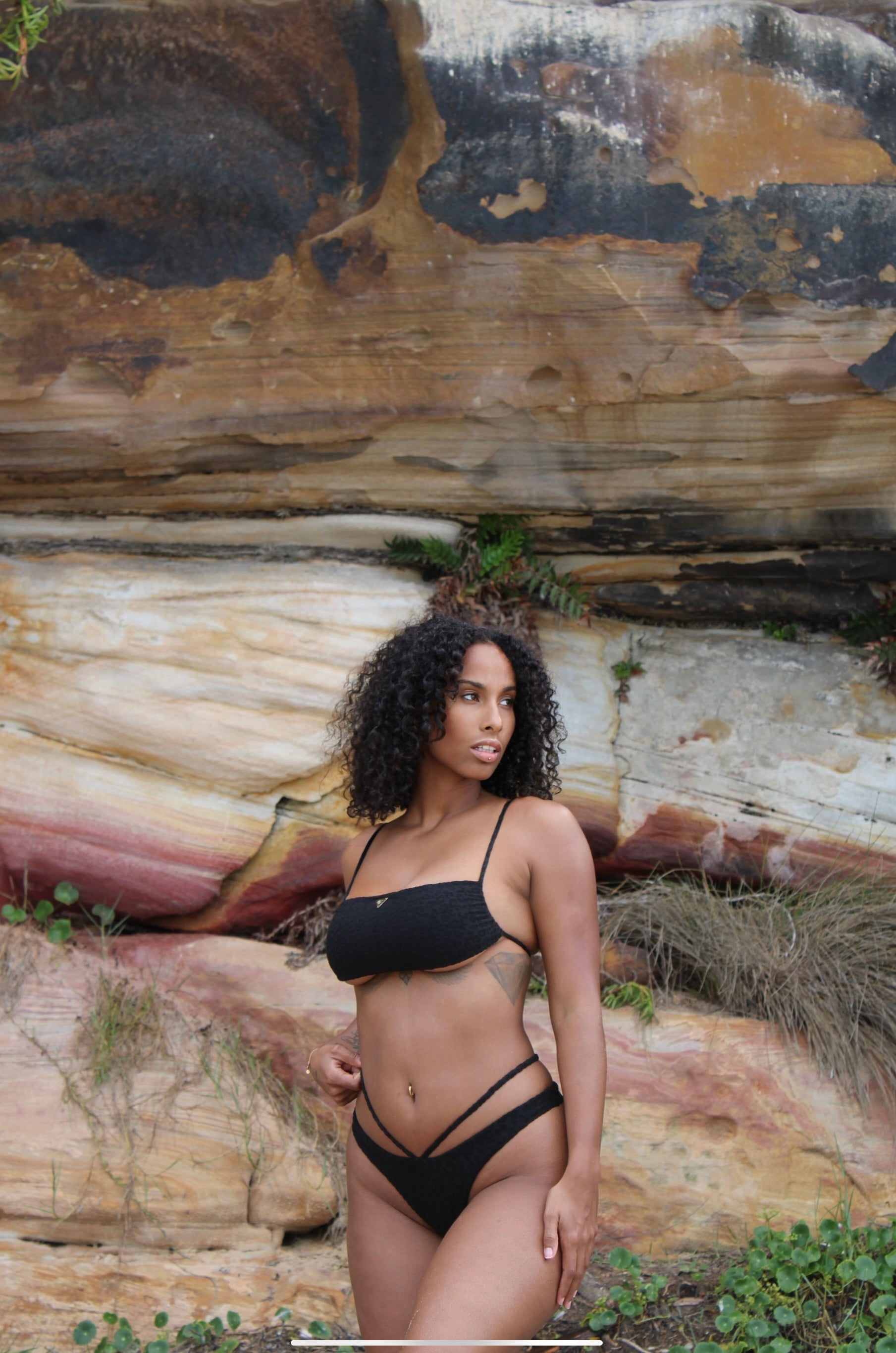 A black textured Leoprint bikini on a woman posing infront of a big natural stone.
