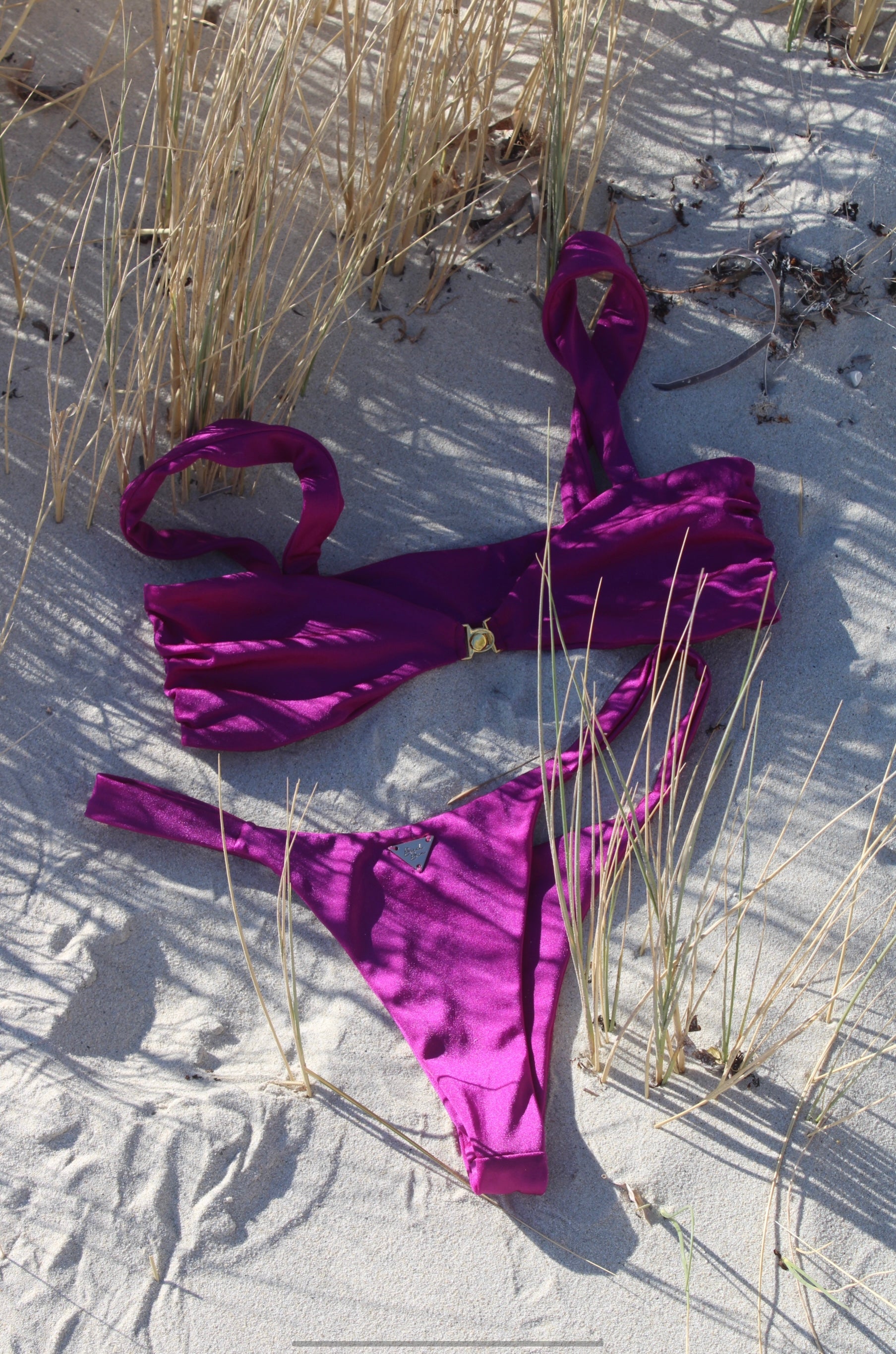 The shiny purple bright Violeta bikini set is lying on the sandy beach.