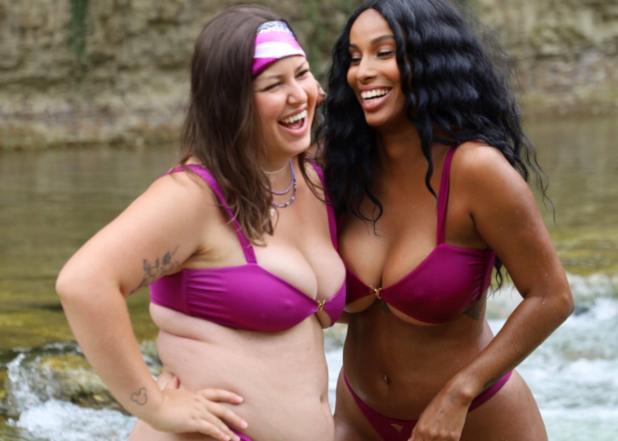Two women in pink bikinis standing by a natural water source.