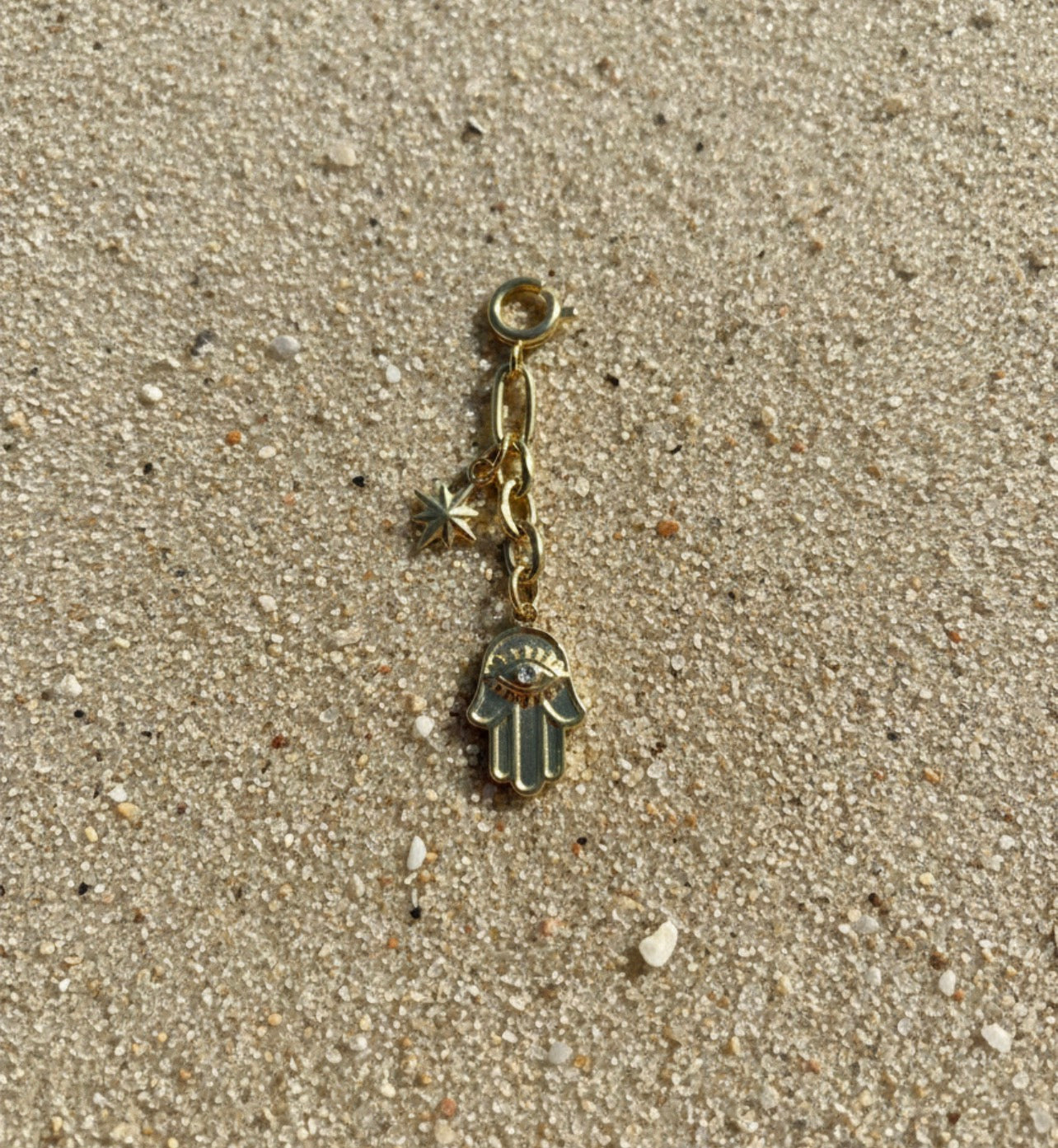 Gold charm with a hamsa hand pendant on a sandy surface