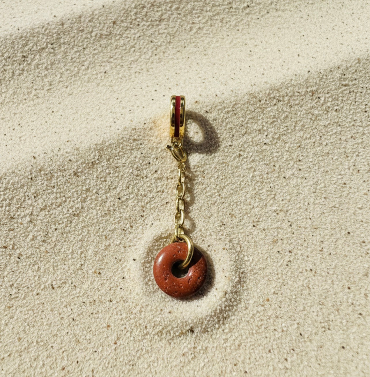 Small gold charm with a red stone on a sandy background