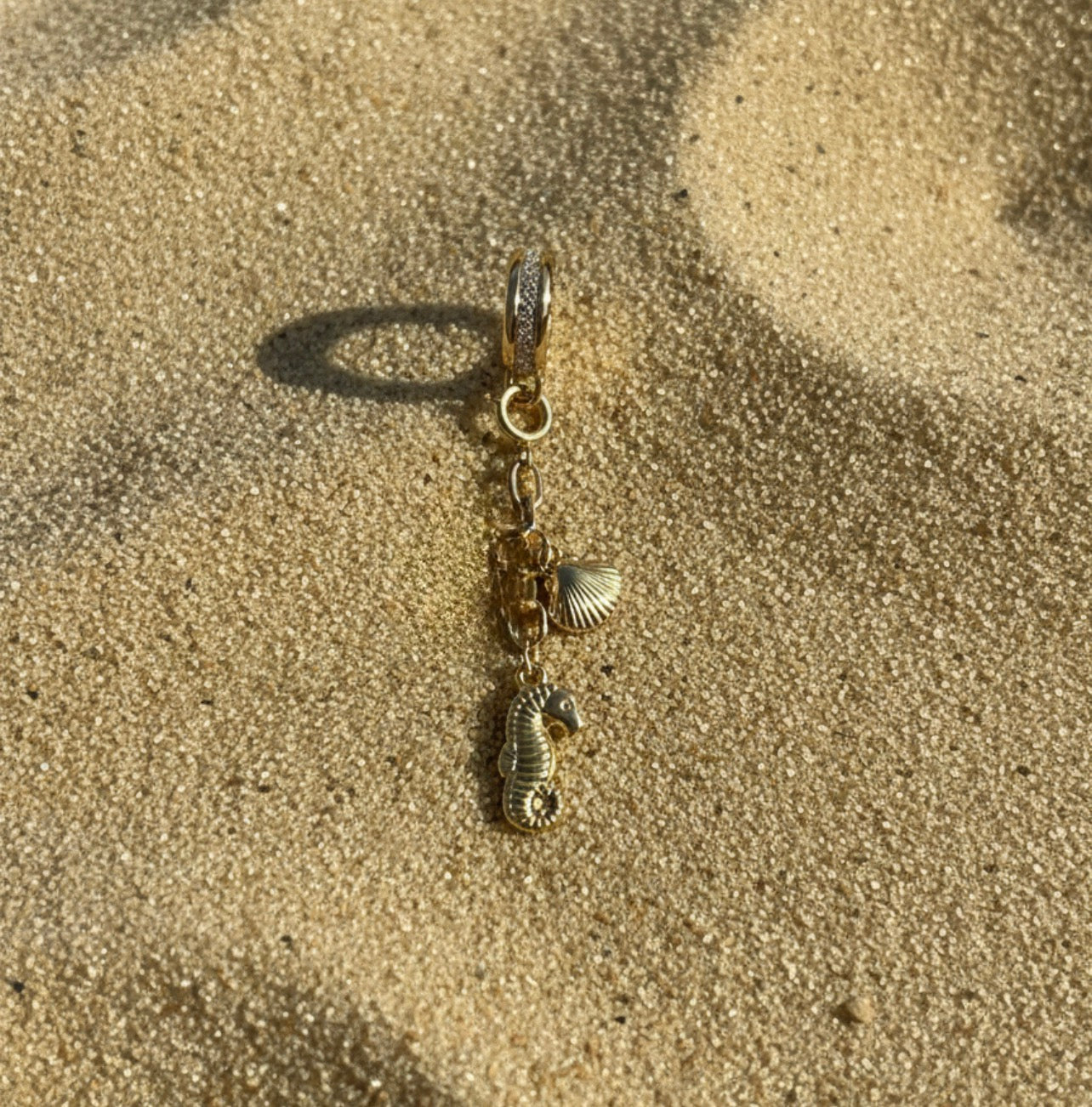 Gold charm with seahorse and shell on sand