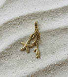 Gold pendant with starfish and seahorse charm on sandy surface